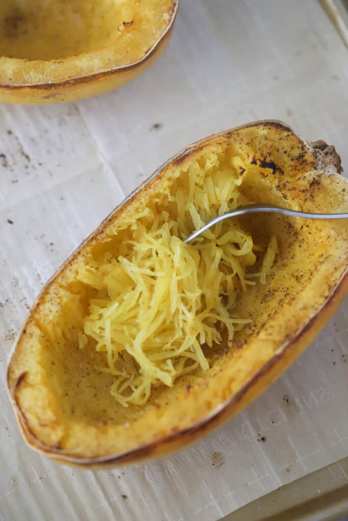 Roasted spaghetti squash with a fork grating the flesh into strands.