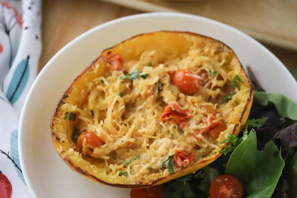 A white plate with half of feta tomato spaghetti squash.