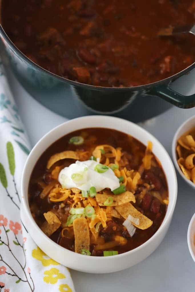 A white bowl full of brisket chili topped with sour cream, cheese, and tortilla strips.