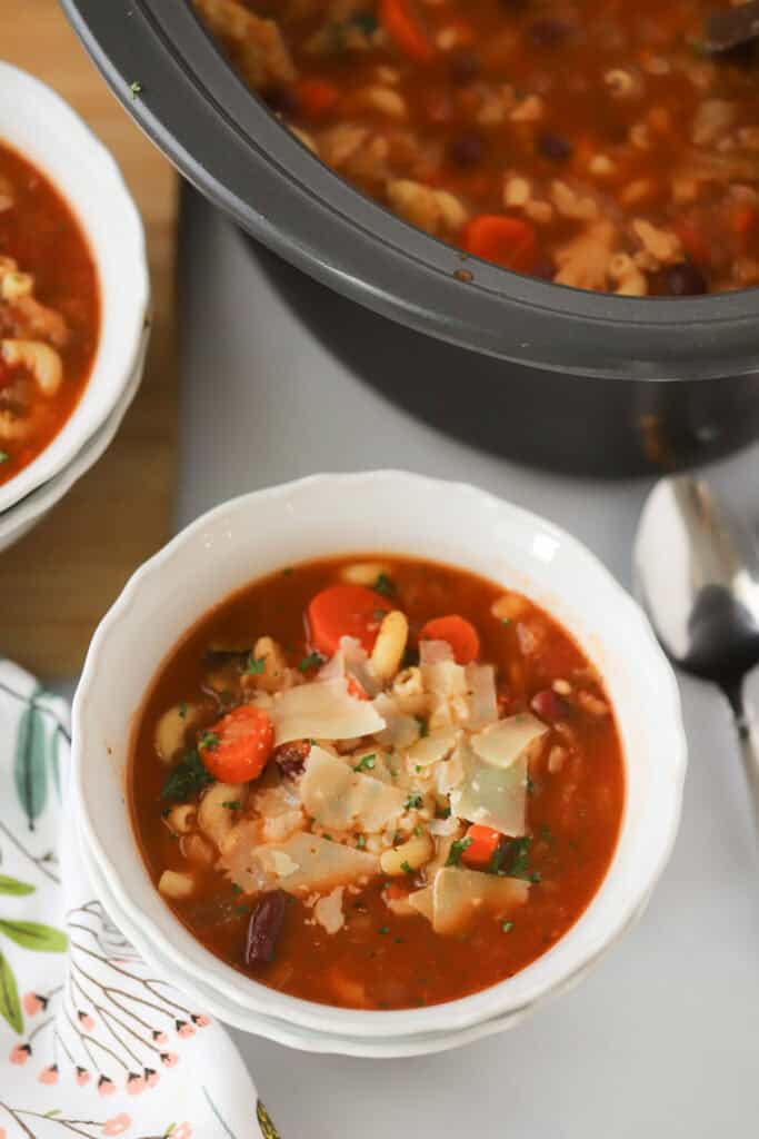 A bowl full of slow cooker minestrone soup with the slow cooker full of soup in the background.