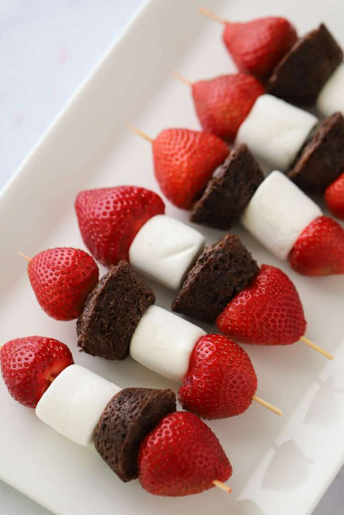 A serving platter with dessert kabobs made from strawberries, brownies, and marshmallows.