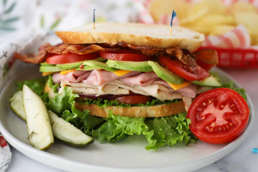 A plate with a turkey club sandwich and a side of pickles.
