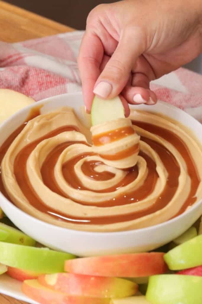 A bowl full of cream cheese caramel apple dip surrounded by apple slices.