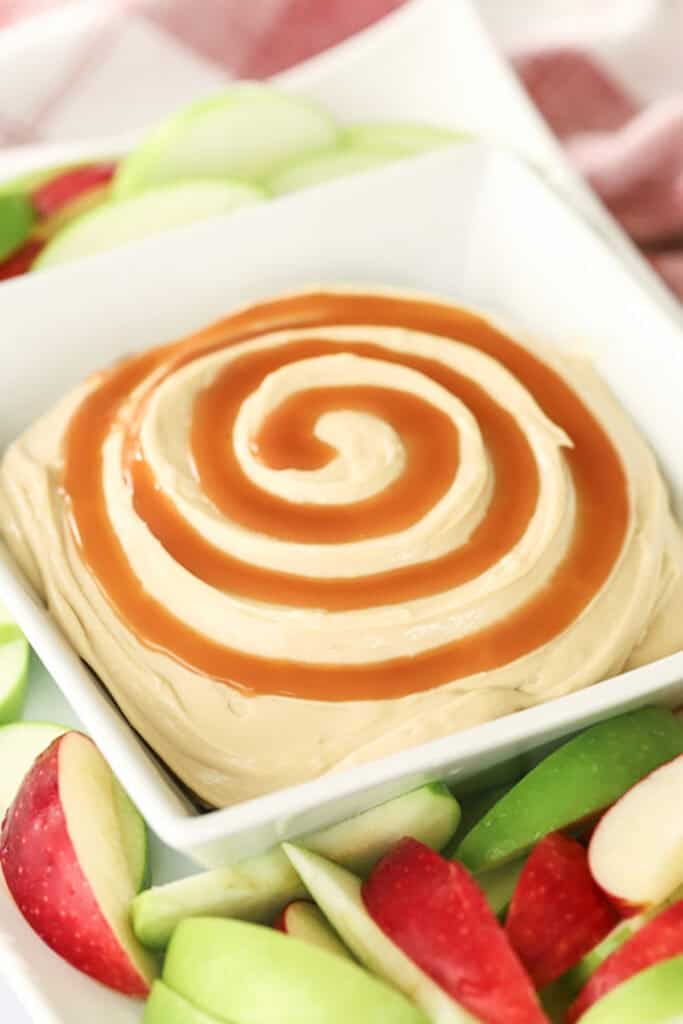 A bowl full of cream cheese apple dip with a spiral of caramel sauce over the top.
